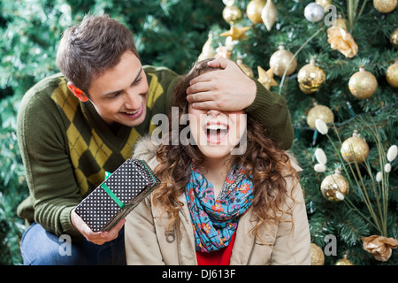 Man Surprising Woman With Gift In Christmas Store Stock Photo