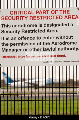 Signs on security fencing at Manchester Airport, UK, with a jet taking off behind. Stock Photo
