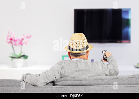 Man with hat sitting on sofa and changing TV channels at home Stock Photo