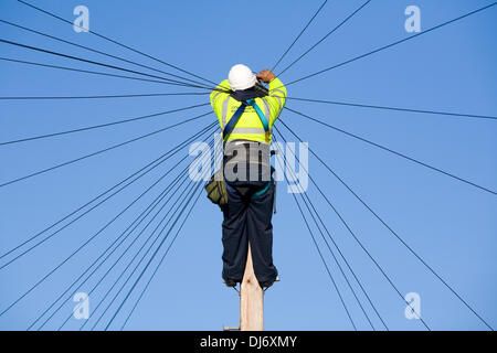 BT plc Telecom engineer (British Telecom PLC) installs a new domestic phone line and broadband internet copper wire to a telephone / telegraph pole in a London Street / Road, under a blue sky. © David Gee 4 Stock Photo