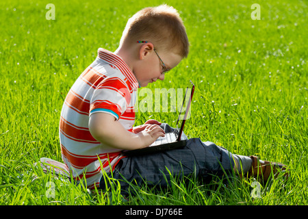 boy using his laptop outdoor in park on grass Stock Photo