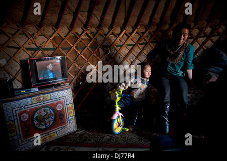 Sep 25, 2012 - Gobi Desert, Mongolia - A herding family sits inside their ger (yurt) with a flat-screen television playing. Most nomad families use portable solar units or windmills to generate electricity and power their electronics. Mongolian pastoral herders make up one of the world's largest remaining nomadic cultures. For millennia they have lived on the steppes, grazing their livestock on the lush grasslands. But today, their traditional way of life is at risk on multiple fronts. Alongside a rapidly changing economic landscape, climate change and desertification are also threatening noma Stock Photo