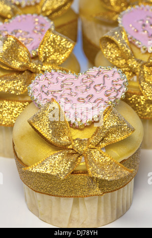 Iced cup cakes decorated with golden bows and pink hearts. Stock Photo