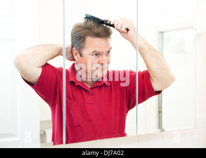 Handsome mature man in his bathroom brushing his hair in the mirror.  Stock Photo