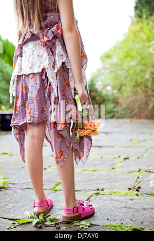 Low section of girl on a warm summers day in a ragged dress, holding a bunch of flowers. Stock Photo