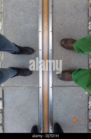 Three pairs of feet straddling (and standing either side of ) the Greenwich Meridian Stock Photo