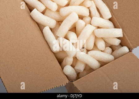 Cardboard box with yellow packing styrofoam peanuts, isolated on white background. Stock Photo