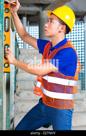 Asian Indonesian builder or craftsman with hardhat, bubble level and pen is controlling or checking a wall of a tower building Stock Photo