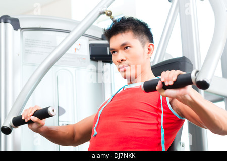 Asian Chinese man having fitness training or workout in gym doing sport to build up muscle on a weight machine Stock Photo