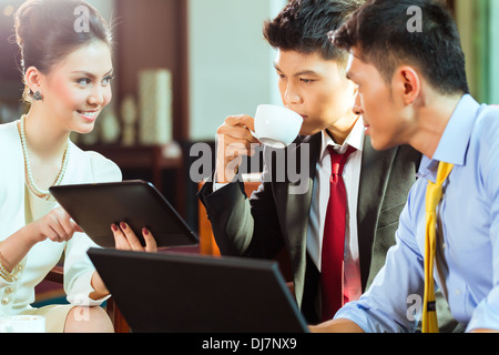 Three Asian Chinese office people or businessmen and businesswoman having a business meeting in a hotel lobby discussing Stock Photo