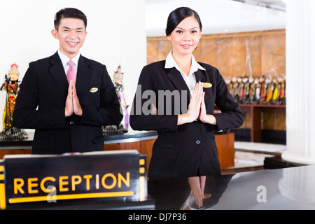 Chinese Asian reception team at luxury hotel front desk welcoming guests with typical gesture, a sign of good service Stock Photo