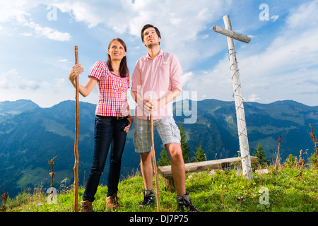 Hiking - Young couple standing on mountain summit at cross in the Bavarian Alps and enjoys the panorama in the leisure time Stock Photo