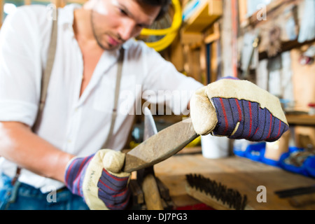Young man in the Bavarian mountains grinds his axe and sharpening tools with a grindstone to chop the fire wood Stock Photo