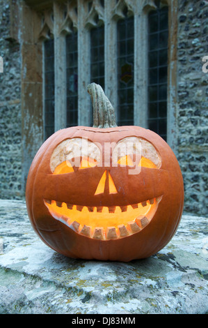 All Hallows Eve. A Halloween Jack o’ Lantern carved from a pumpkin, glowing by candlelight, in an ancient churchyard. England, United Kingdom. Stock Photo