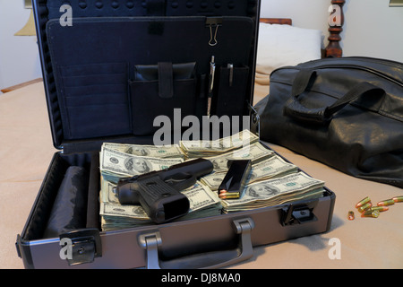 An automatic pistol and clip on stacks of U.S. 100 dollar bills in a briefcase on a bed. Bullets and luggage are beside the case Stock Photo