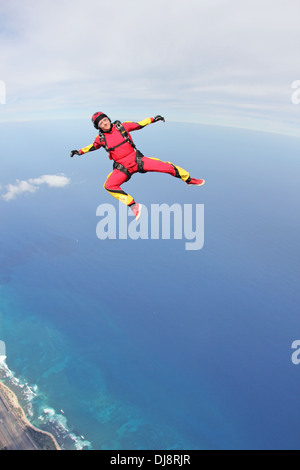 This skydiver girl is flying in a free style position over the deep blue sea next to the shore line with high speed of 120 MPH. Stock Photo