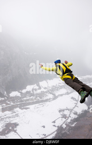 BASE jumper is exiting from a cliff down into the deep valley. Thereby he's keeping his arms up to be stable and save. Stock Photo