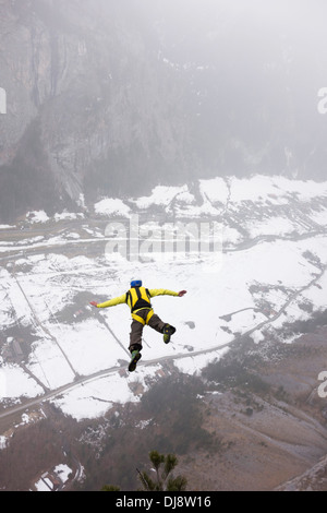 BASE jumper is exiting from a cliff down into the deep valley. Thereby he's keeping his arms up to be stable and save. Stock Photo