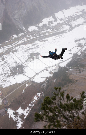 BASE jumper is exiting from a cliff down into the deep valley. Thereby he's keeping his arms up to be stable and save. Stock Photo