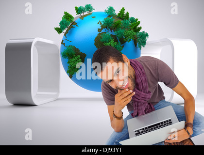 Composite image of thoughtful man sitting on floor using laptop and smiling at camera Stock Photo