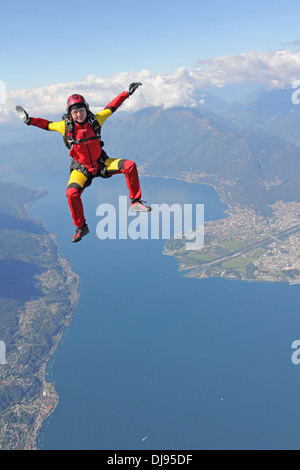 This skydiver woman is falling free in a sit position over a big lake next to a beautiful mountain area. Stock Photo
