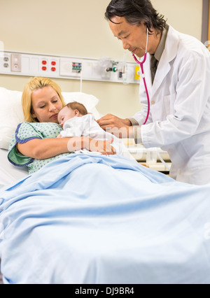 Doctor Examining Babygirl Sleeping In Mother's Arms Stock Photo