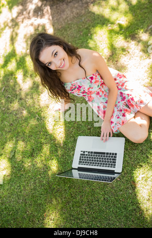 Stylish gorgeous brunette sitting on the grass using laptop Stock Photo