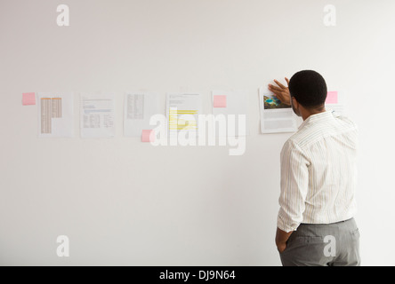 Black businessman taping up papers on office wall Stock Photo