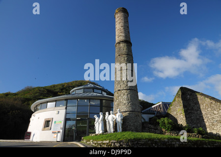 A ruined chimney with a group of sculptured figures of miners and a modern building behind. Stock Photo