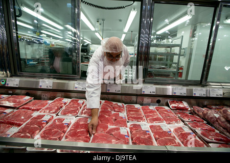 Hispanic employee wearing food safety hair net stocks with fresh meat department at a newly open COSTCO warehouse retail store Stock Photo