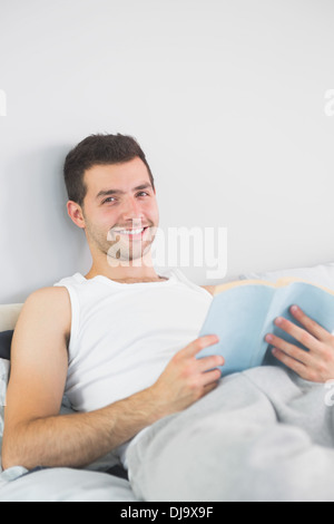 Handsome smiling man reading book in his bed Stock Photo