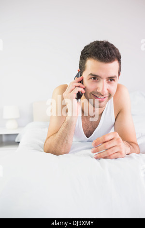 Smiling handsome man lying in bed phoning Stock Photo