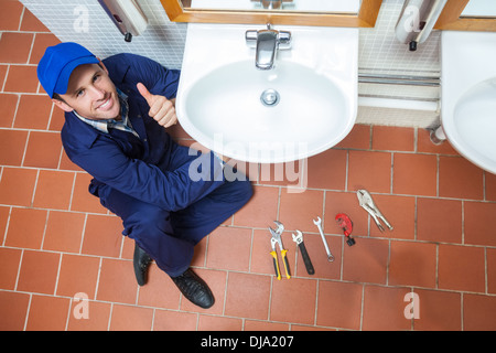 Cheerful plumber repairing sink showing thumb up Stock Photo