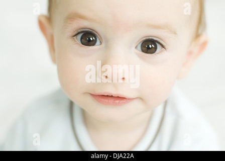 A baby boy with huge brown eyes smiles innocently, white background. Stock Photo