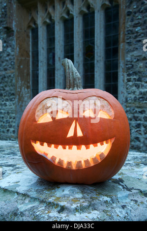 All Hallows Eve. A Halloween Jack o’ Lantern carved from a pumpkin, glowing by candlelight, in an ancient churchyard. England, United Kingdom. Stock Photo