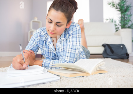 Gorgeous brunette student doing homework lying on the floor Stock Photo