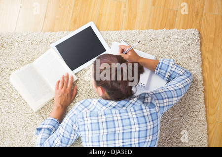 Brunette female student lying on the floor doing assignments Stock Photo