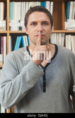 Male librarian making a sign to be quiet in library Stock Photo