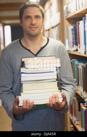 Handsome brunette librarian posing in library holding a pile of books Stock Photo