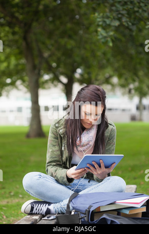 Focused brunette student using tablet sitting on bench Stock Photo