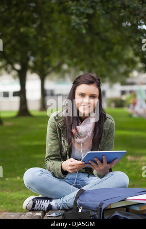 Smiling brunette student using tablet sitting on bench Stock Photo