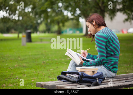 Serious casual student sitting on bench taking notes Stock Photo