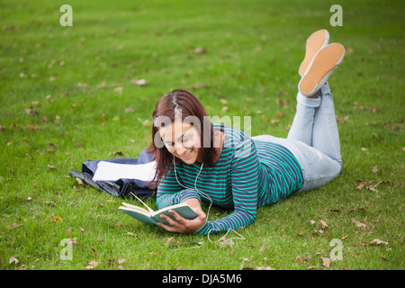 Happy casual student lying on grass reading Stock Photo