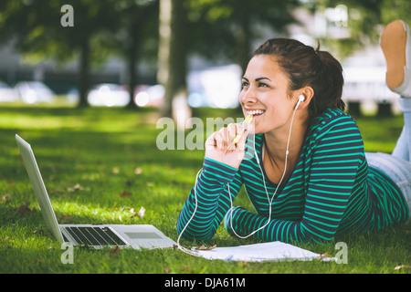 Laughing casual student lying on grass taking notes Stock Photo