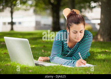 Calm casual student lying on grass taking notes Stock Photo
