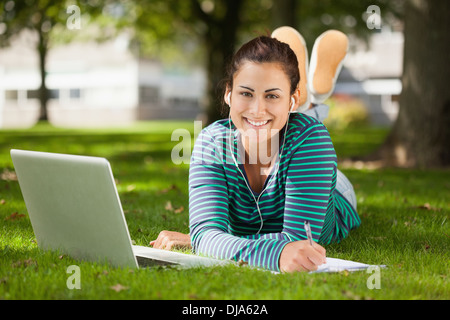 Happy casual student lying on grass taking notes Stock Photo