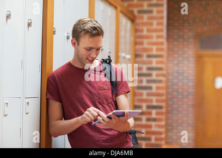 Handsome student leaning against lockers using tablet Stock Photo