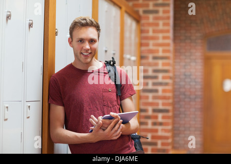 Handsome smiling student leaning against lockers using tablet Stock Photo
