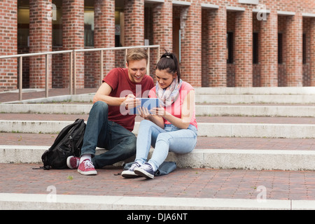 Happy students sitting on stairs using tablet Stock Photo