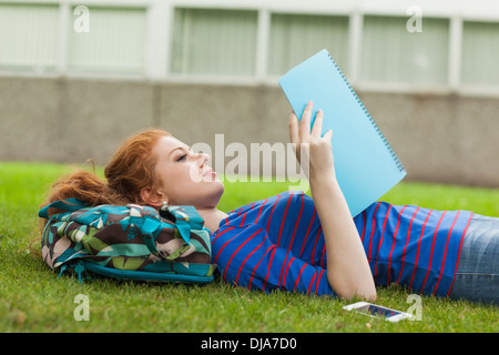 Gorgeous concentrating student lying on grass reading notes Stock Photo